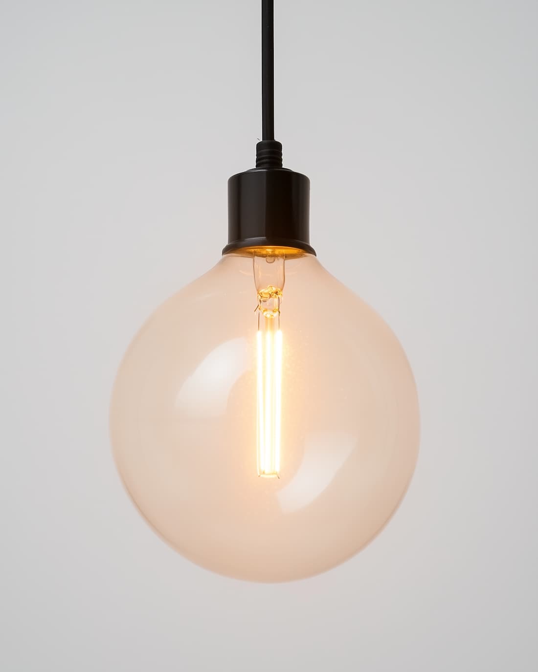 A pendant light with an exposed filament bulb hanging on a black cord above the tables.